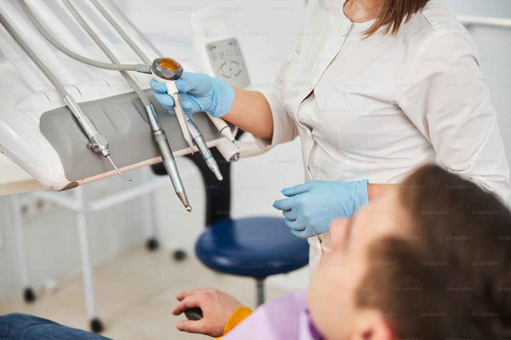 Medical person picking a stomatological handpiece attached to instrument unit while preparing for treating patient