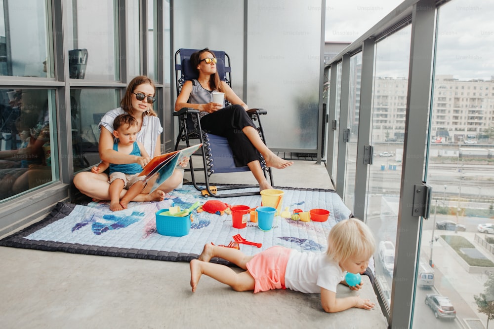 Young mothers spending time together with children babies on balcony at home. Staycation during coronavirus covid-19 pandemic in the world. Preventive measures against virus spread.