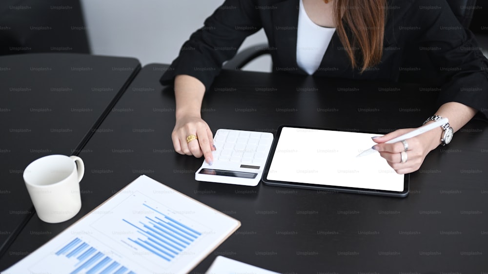 Cropped shot of young woman accountant using digital tablet and calculate business data.