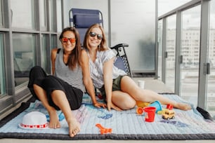 若いレズビアンLGBTQの女性の家族は、自宅のバルコニーで一緒に時間を過ごしています。サングラスをかけた女性に微笑む幸せな女性。世界でのコロナウイルスcovid-19パンデミック中のステイケーション。
