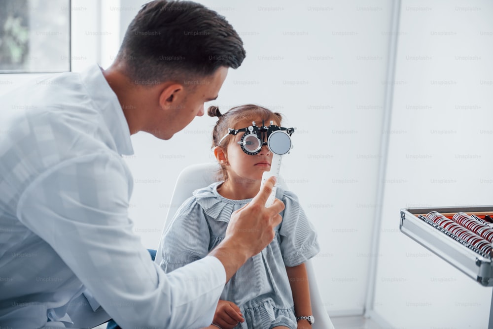 Sehkraft testen. Junge Augenärztin ist mit wenig weiblichem Besucher in der Klinik.