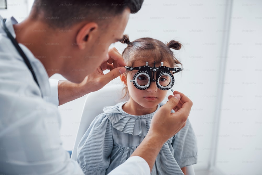 Testing vision. Young ophthalmologist is with little female visitor in the clinic.