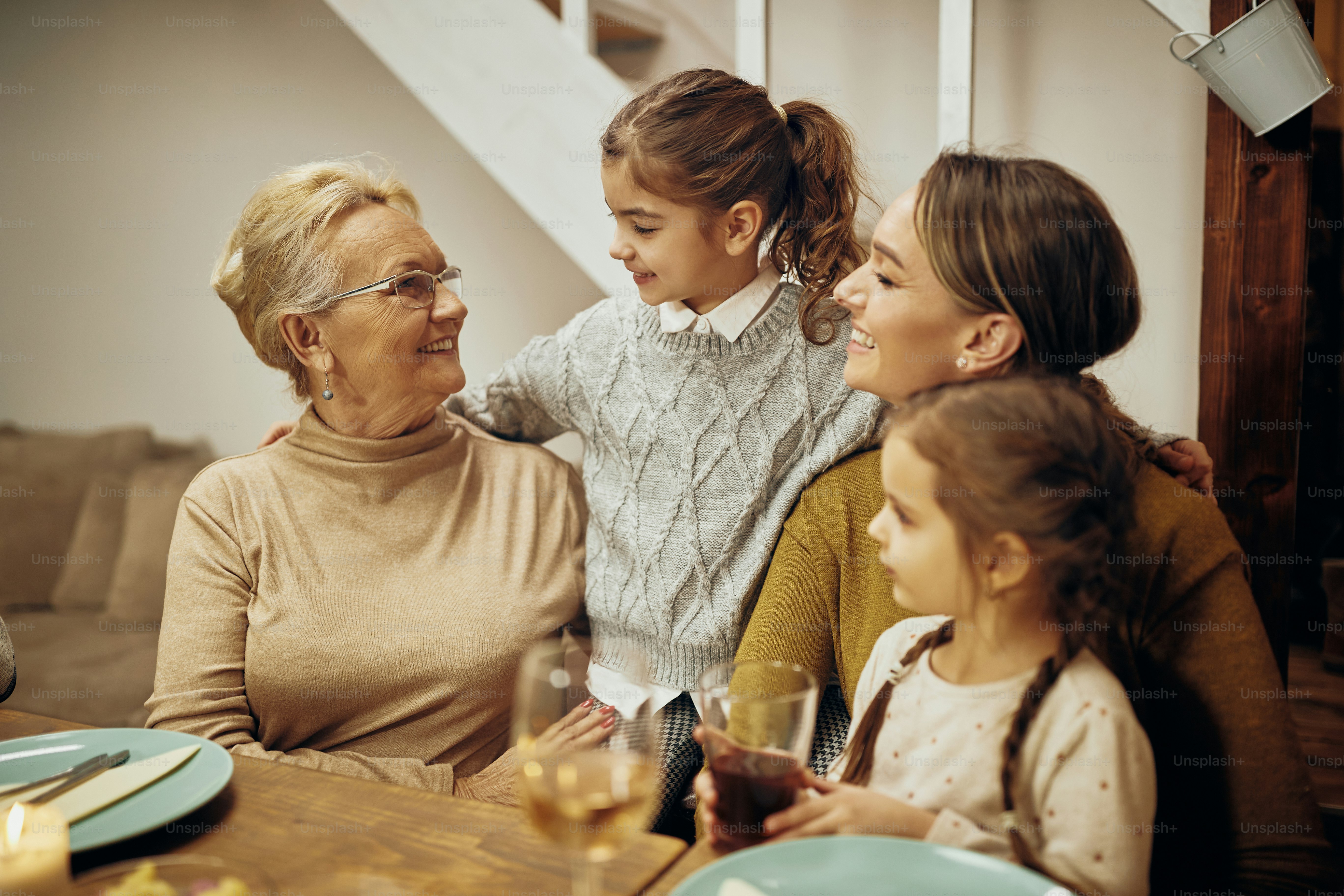 Happy senior woman communicating with her granddaughters and daughter at dining table.