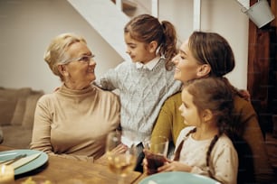 Happy senior woman communicating with her granddaughters and daughter at dining table.