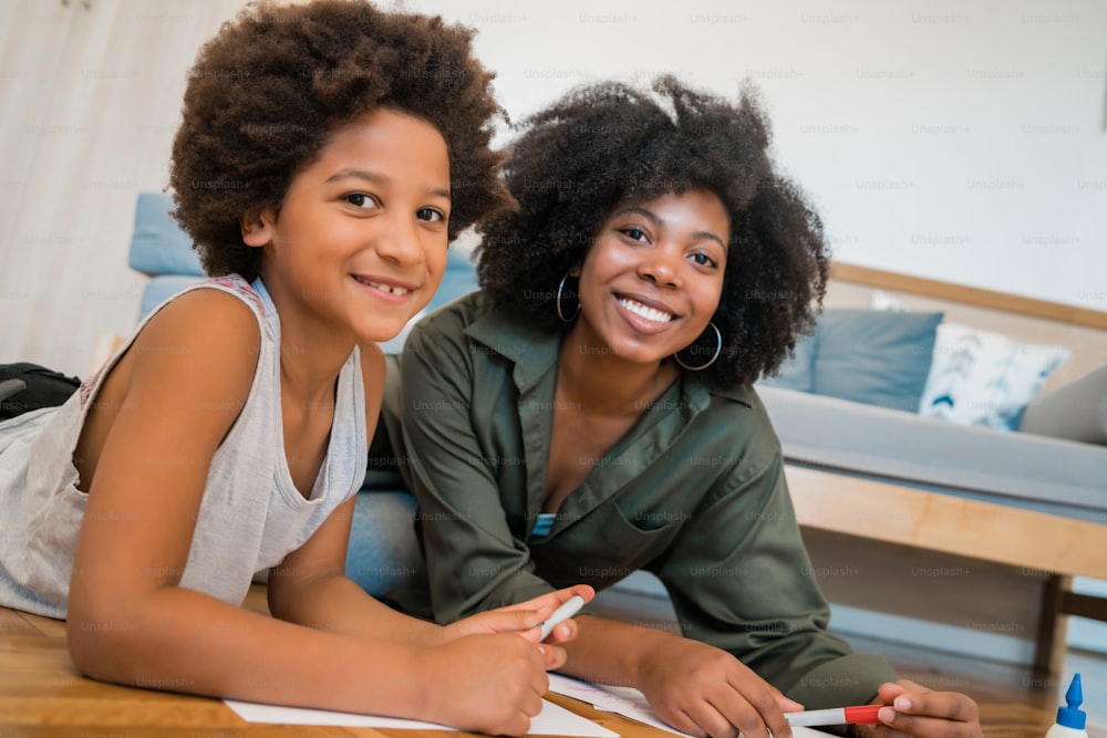 Portrait d’une jeune mère afro-américaine et son fils dessinant avec des crayons de couleur sur un sol chaud à la maison. Concept familial.