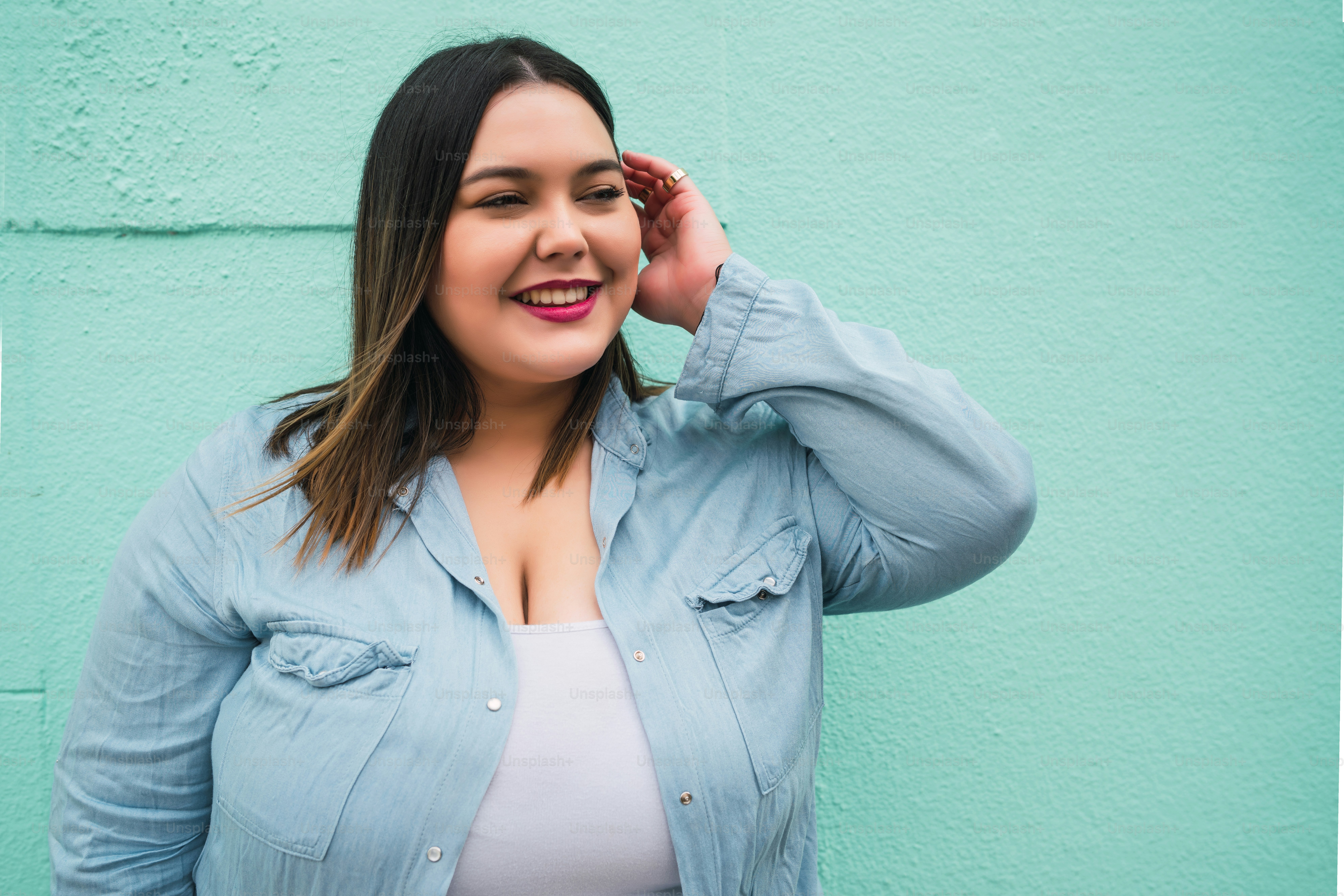 Close-up of young plus size woman smiling while standing against light blue wall outdoors. Urban concept.