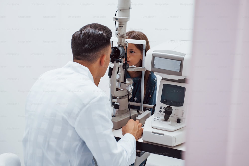 Young ophthalmologist is with little female visitor in the clinic.