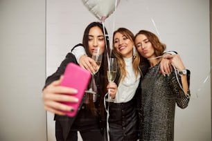 Vista frontal de amigas borrachas con copas de champán y globos posando para la cámara