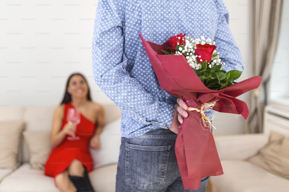 Happy woman looking at her boyfriend holding bouquet of roses behind his back. Man holding flowers behind his back to surprise his girlfriend, romantic happy couples on 8 March happy women's day