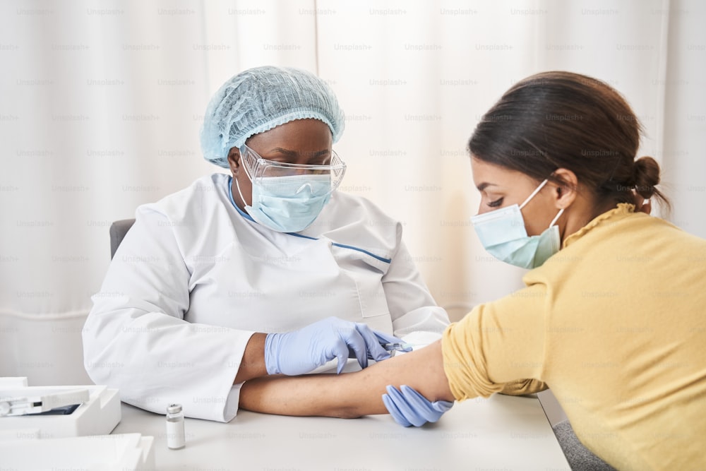 若い女性に予防接種を行う医療顧問の接写。若い女性に注射を打つ準備をしている医師の接写で、彼女はテーブルに腕を置いています。ストックフォト