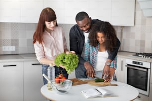 Waist up portrait of the happy young father teaching his teenage daughter holding knife and cut fresh vegetables in kitchen interior. Cute little girl learning cooking while preparing salad