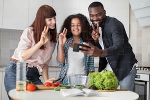 Good selfie. Joyful mixed rac daughter standing at the table in the kitchen and taking a selfie with her mom and dad, all of them are happy and laughing. Stock photo