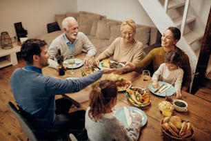 Happy extended family having dinner at dining table at home. Focus is on young woman passing food to her husband.