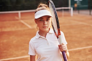 Portrait of young female tennis player in sportive clothes is on the court outdoors.