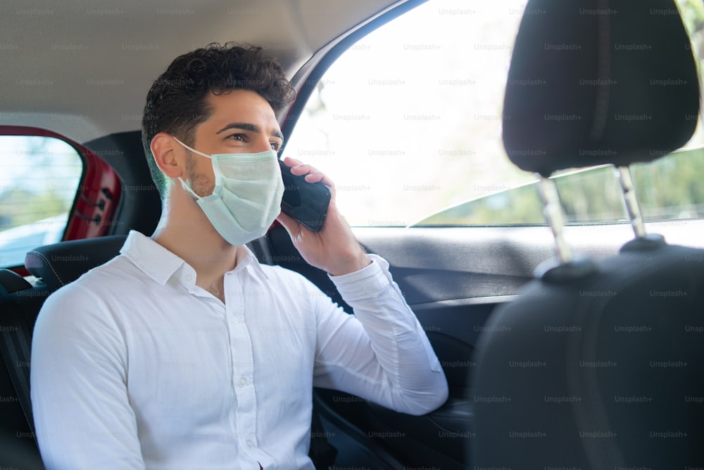 Portrait of businessman wearing face mask and talking on phone on way to work in a car. Business concept. New normal lifestyle concept.