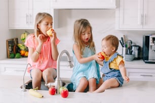 Kaukasische Kindermädchen, die frisches Obst essen, sitzen in der Küchenspüle. Glückliche Familienschwestern Geschwister beim Snack. Bio-Lebensmittel gesunde, leckere leckere Mahlzeit für Kinder. Lifestyle authentischer Moment
