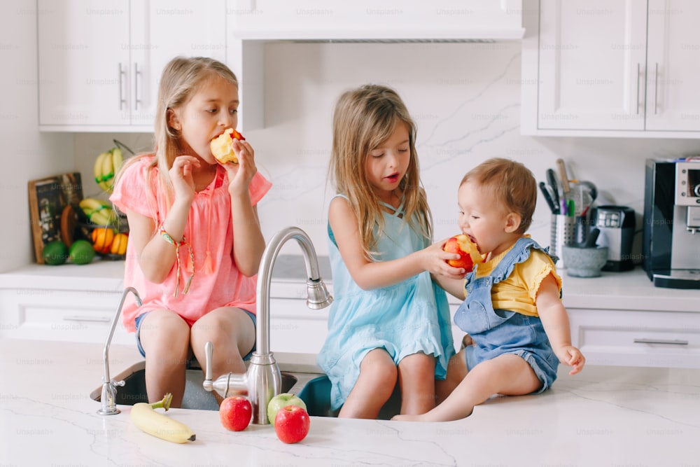 Crianças caucasianas comendo compartilhando frutas frescas sentadas na pia da cozinha. Irmãos felizes da família fazendo lanche. Alimentos orgânicos saudáveis deliciosa refeição saborosa para as crianças. Momento autêntico do estilo de vida