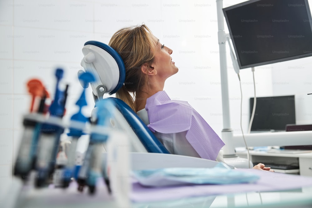 Calm woman patient leaning back on dentist chair and staring at black screen in front of her