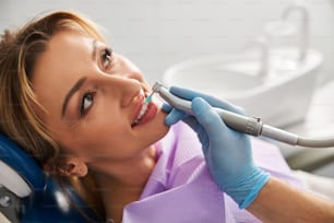 Hand hält einen Zahnbohrer mit einem blauen Prophy-Becher auf Bohrerpolierzähnen der Frau