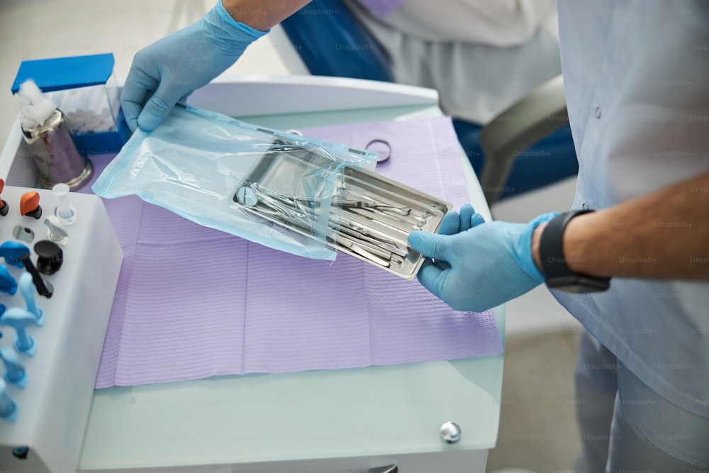 Medical worker removing a steel tray with stomatological tools inside from a poly self sealing bag