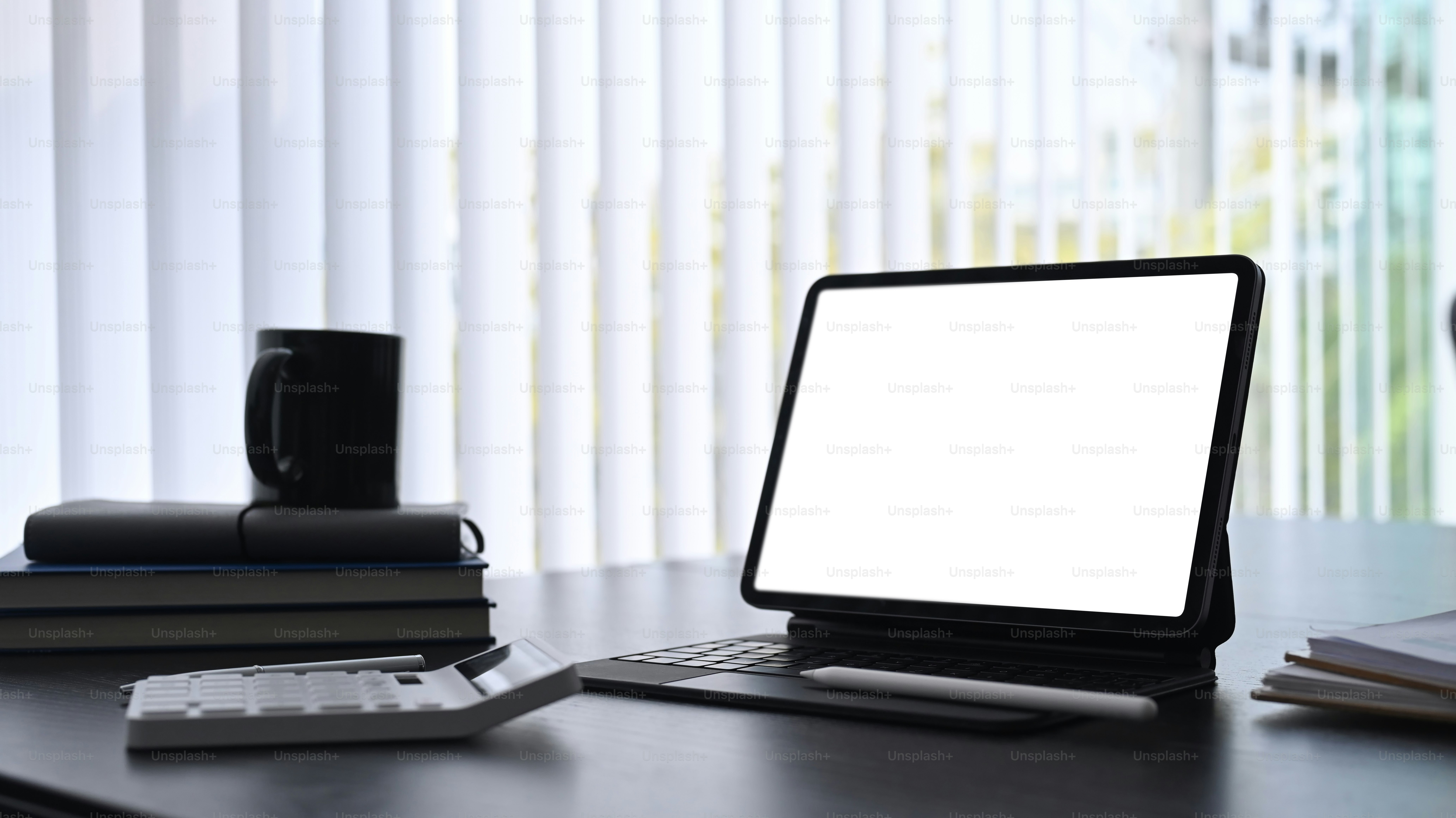 Accountant workplace with computer tablet, books calculator and coffee cup on dark modern office desk.
