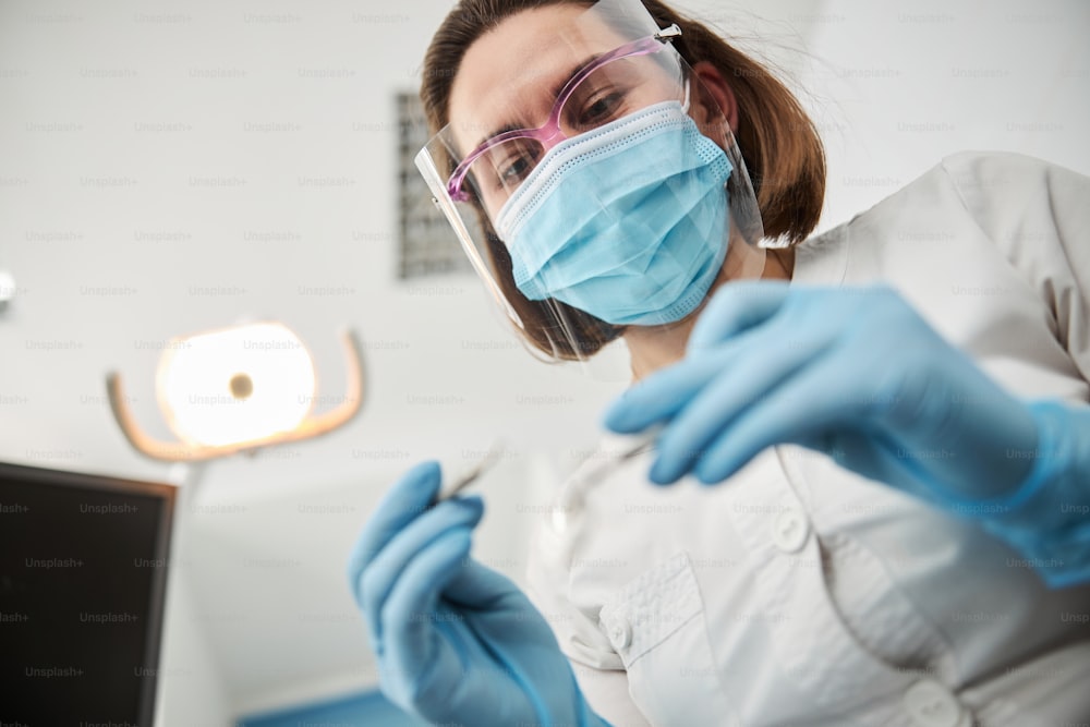 Woman wearing protective equipment on her face and hands looking down at dental appliance