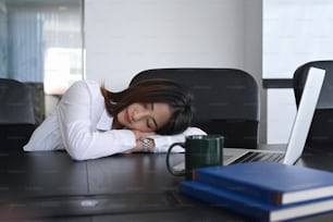 Joven oficinista asiática cansada de trabajar y tomar una siesta en su escritorio.