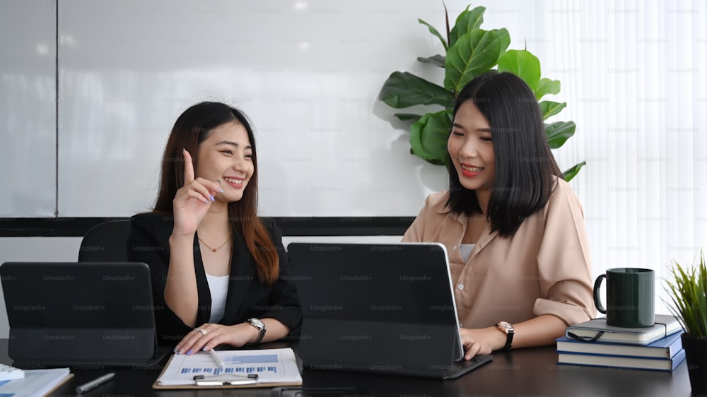 Duas jovens empresárias trabalhando com tablet de computador e discutindo projeto no escritório.