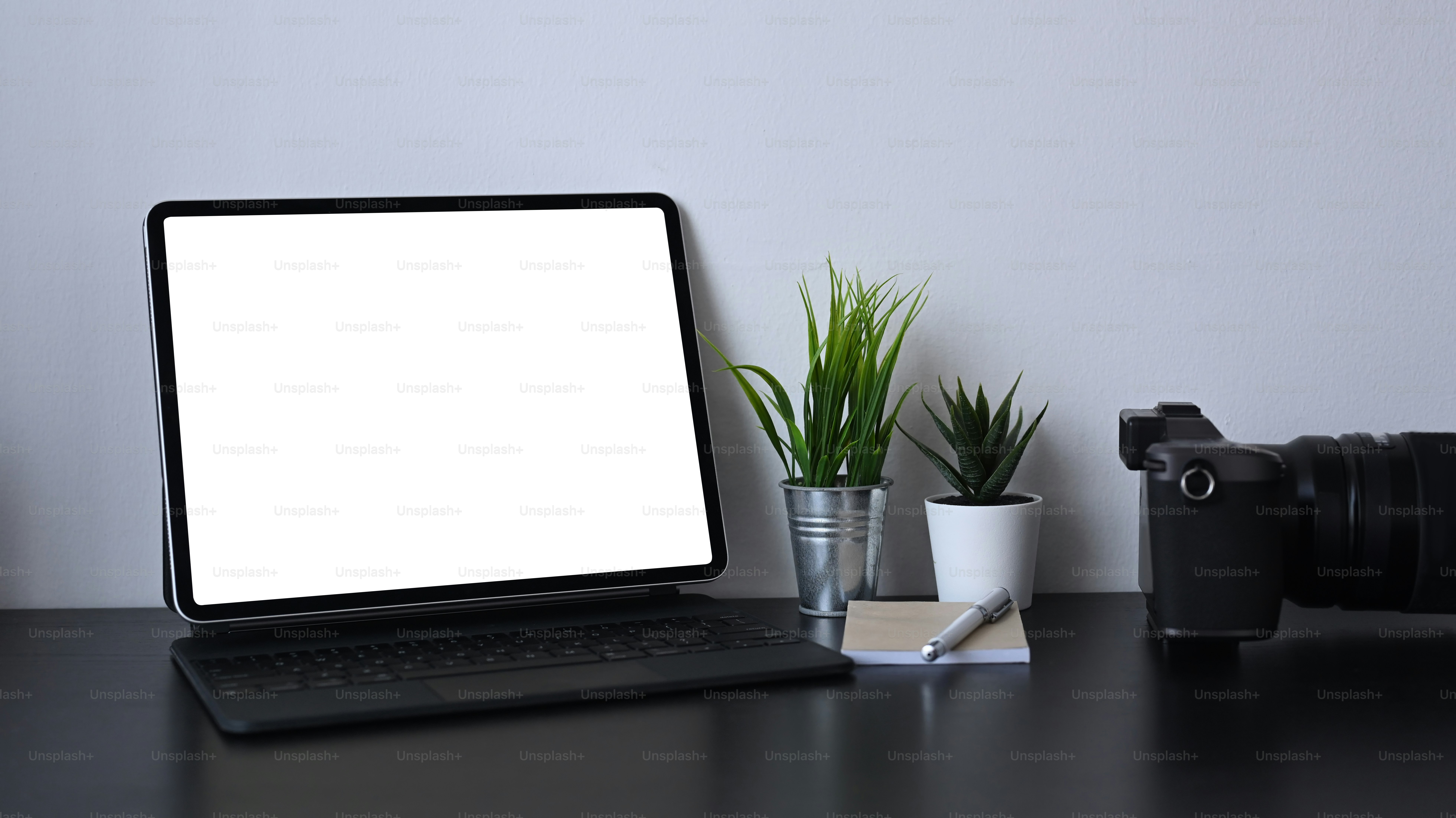 Mock-up-Computer-Tablet mit leerem Bildschirm, Zimmerpflanze und Kamera auf schwarzem Tisch.