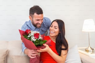 Excited young woman receiving unexpected Bouquet of red roses from husband at home, loving generous boyfriend making romantic surprise to attractive girlfriend on Valentines day occasion