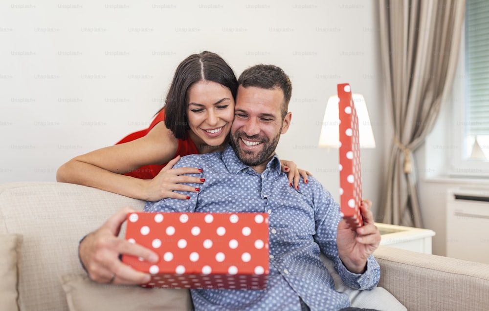 Beautiful smiling young couple celebrating love for birthday or anniversary. Attractive woman surprising him with a present.
