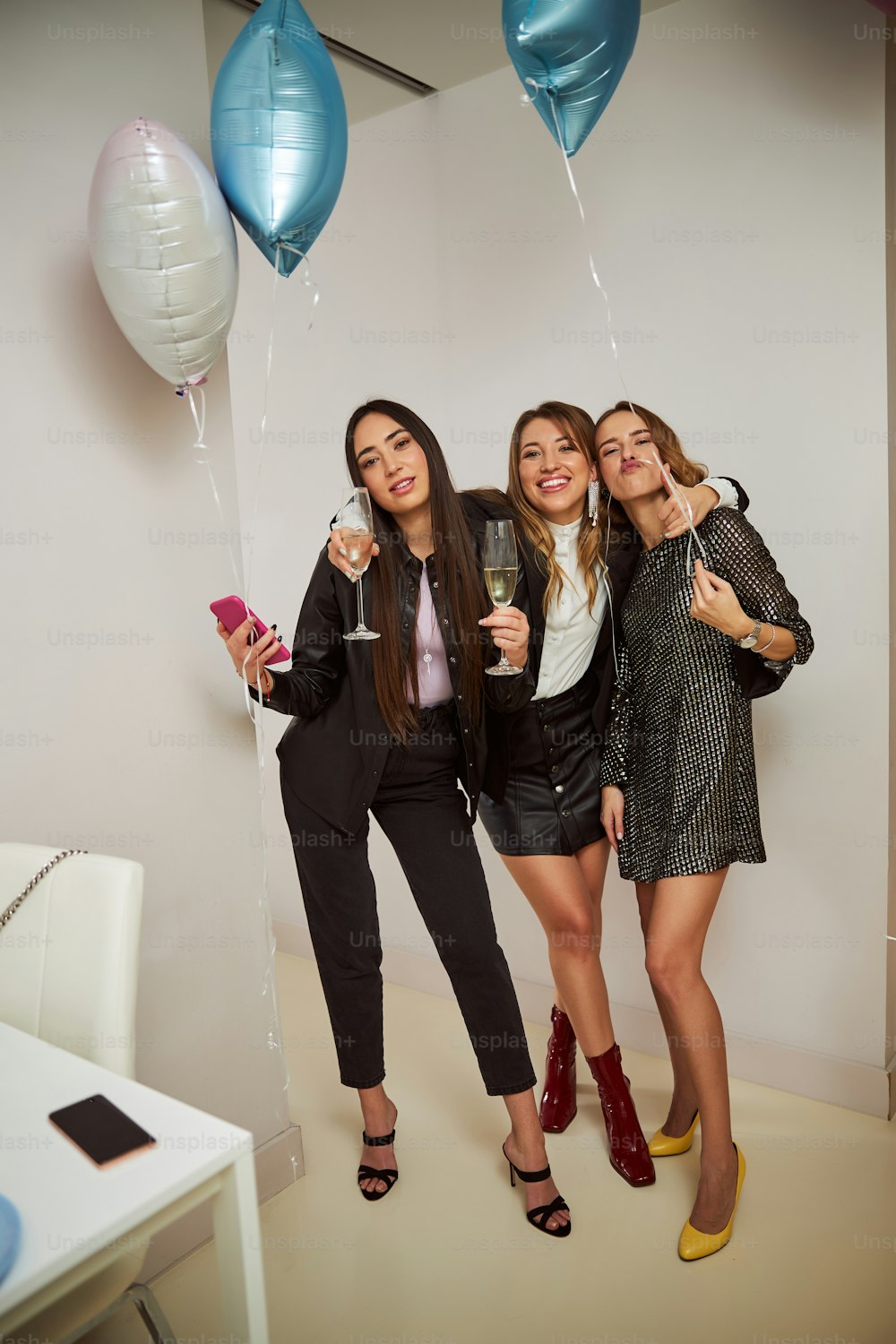 Full-sized portrait of a cheerful slim birthday girl hugging her stylish female friends with balloons