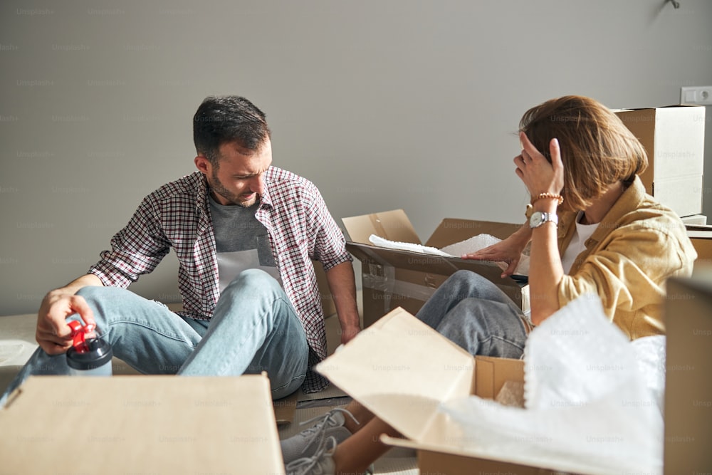 진지한 집중된 남자와 금발의 백인 여자가 새 아파트의 바닥에 앉아 있다