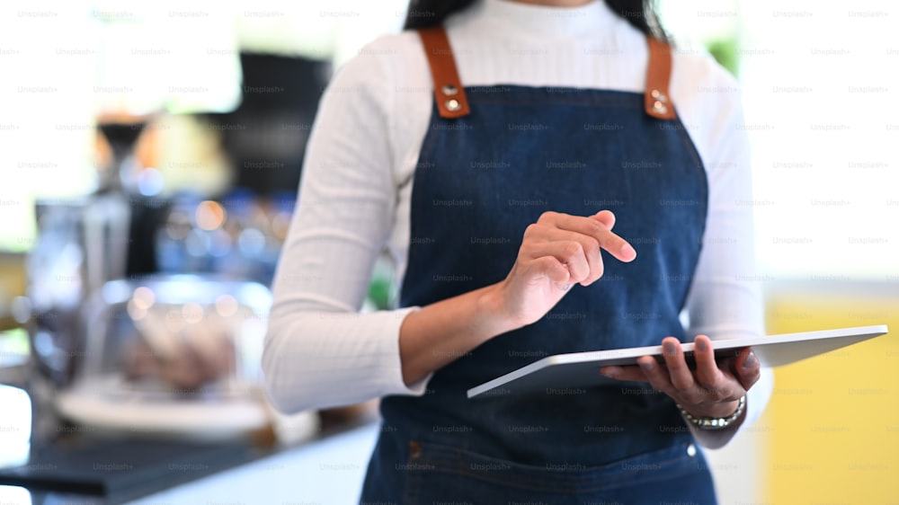 Foto cortada de mulher pequena empresária usando tablet digital e em pé na frente do balcão bar na cafeteria.
