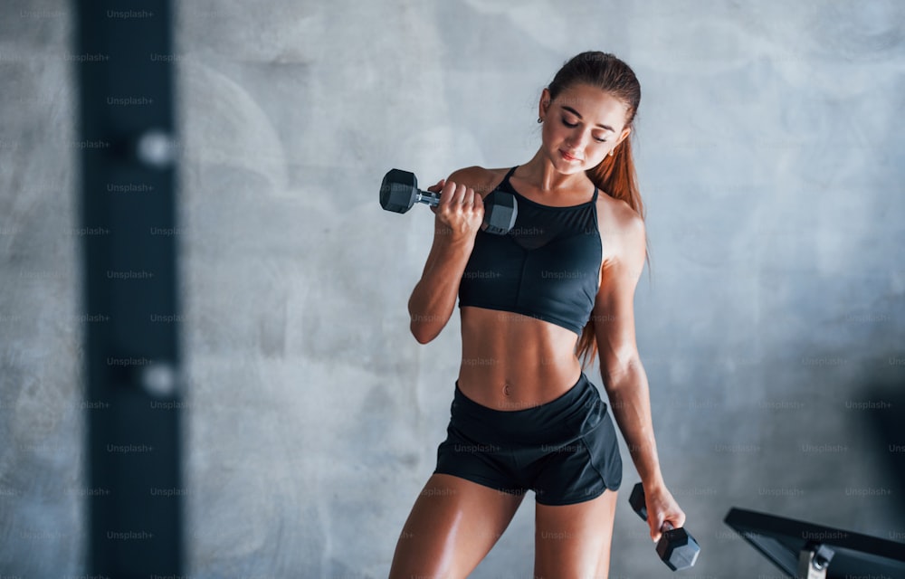 Young fitness woman is in the gym with dumbbells in hands.