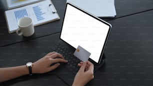 Businesswoman hand holding credit card and using computer tablet shopping online or internet banking at her office desk.