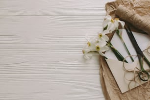 工芸品の封筒とハサミの美しい水仙、テキスト用のスペースを持つ白い素朴な木製の背景にひも。母の日おめでとう。女性の日おめでとう。