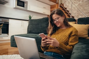 Shot of a young woman using her laptop and a smartphone while sitting on a floor at home