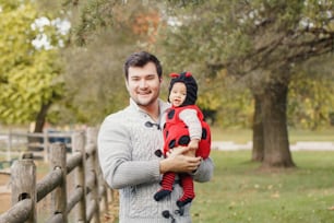 てんとう虫の衣装を着たかわいい愛らしい女の赤ちゃんと幸せな笑顔の白人の父のお父さん。秋の秋の公園の屋外の家族。ハロウィーンの休日の季節のコンセプト。