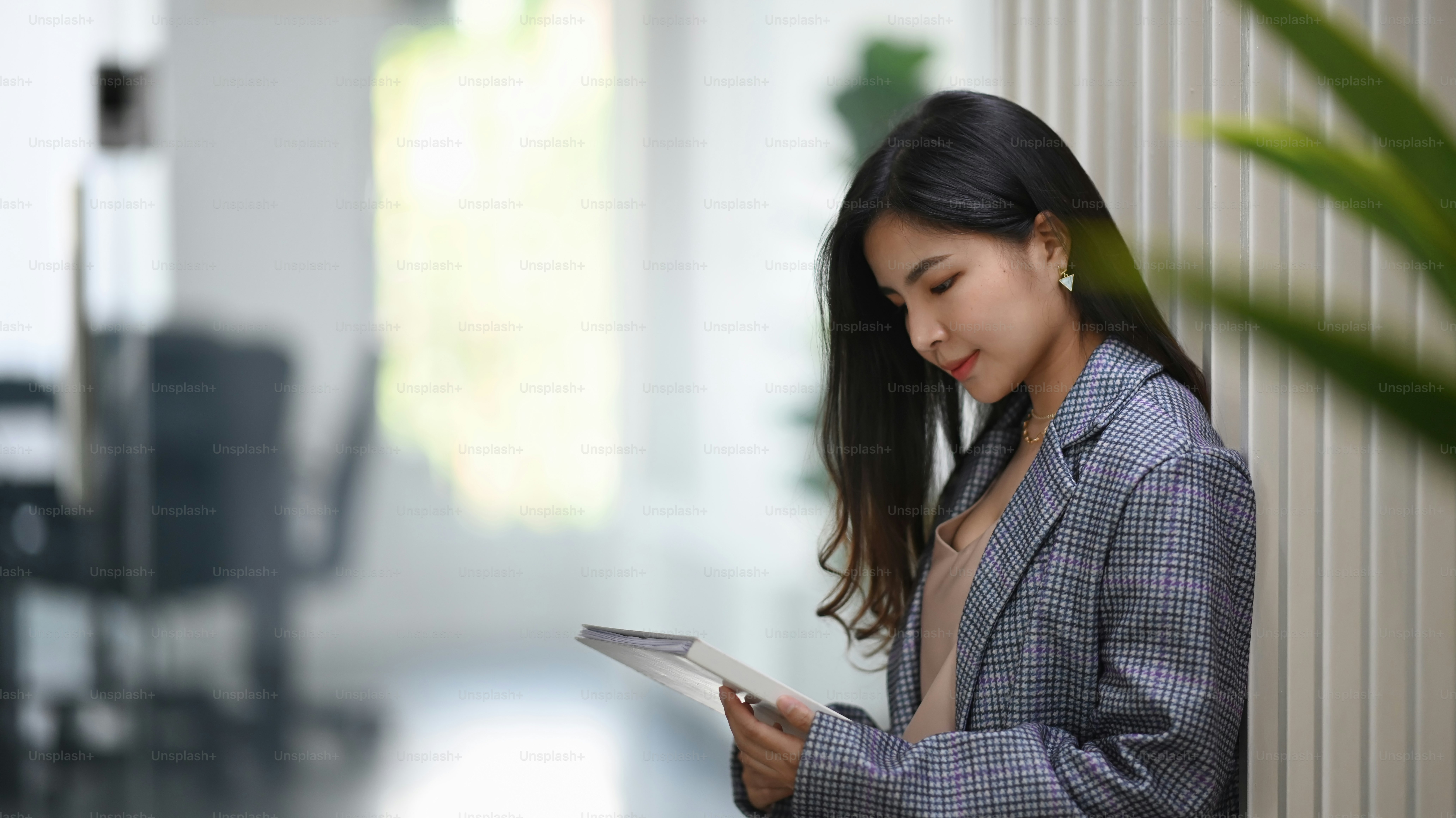 Confident businesswoman reading information in folder while standing at office corridor.