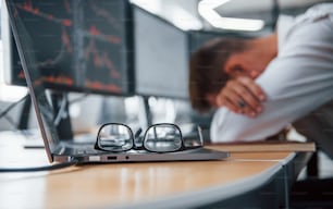 Tired businessman sleeping on the workplace by leaning on the table with multiple screens on it. Stock information on displays.