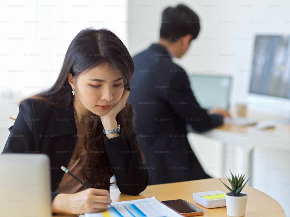 Portrait of businesswoman concentrating on paperwork while working in office room with coworker in background