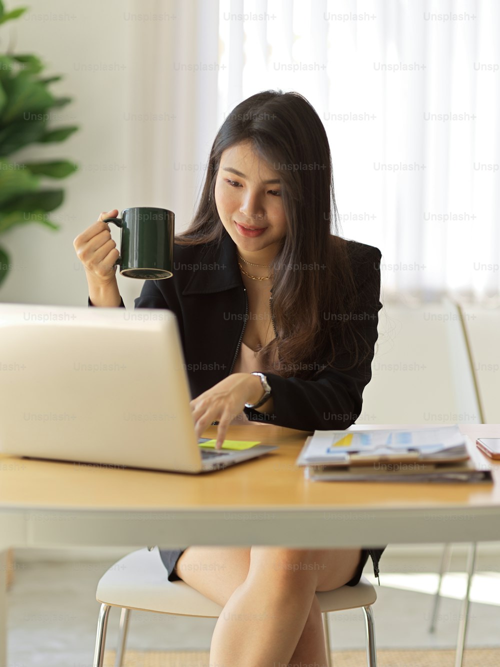 Portrait of businesswoman holding coffee cup and working with laptop in modern office room