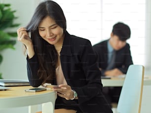 Portrait of businesswoman looking on credit card in her hand while online paying on smartphone