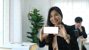 Cheerful businesswoman holding and showing mobile phone with blank black screen.  Blank screen for graphics display montage.