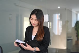 Mujer de negocios sonriente leyendo información en un cuaderno mientras está de pie en la oficina.