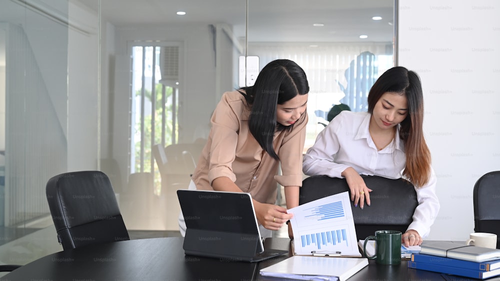 Two businesswoman sharing ideas and preparing presentation in modern meeting room.