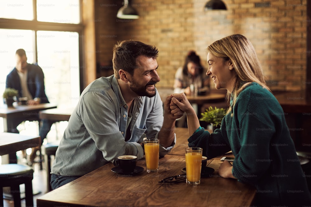 Pareja feliz comunicándose y tomados de la mano mientras están en una cita en un café.