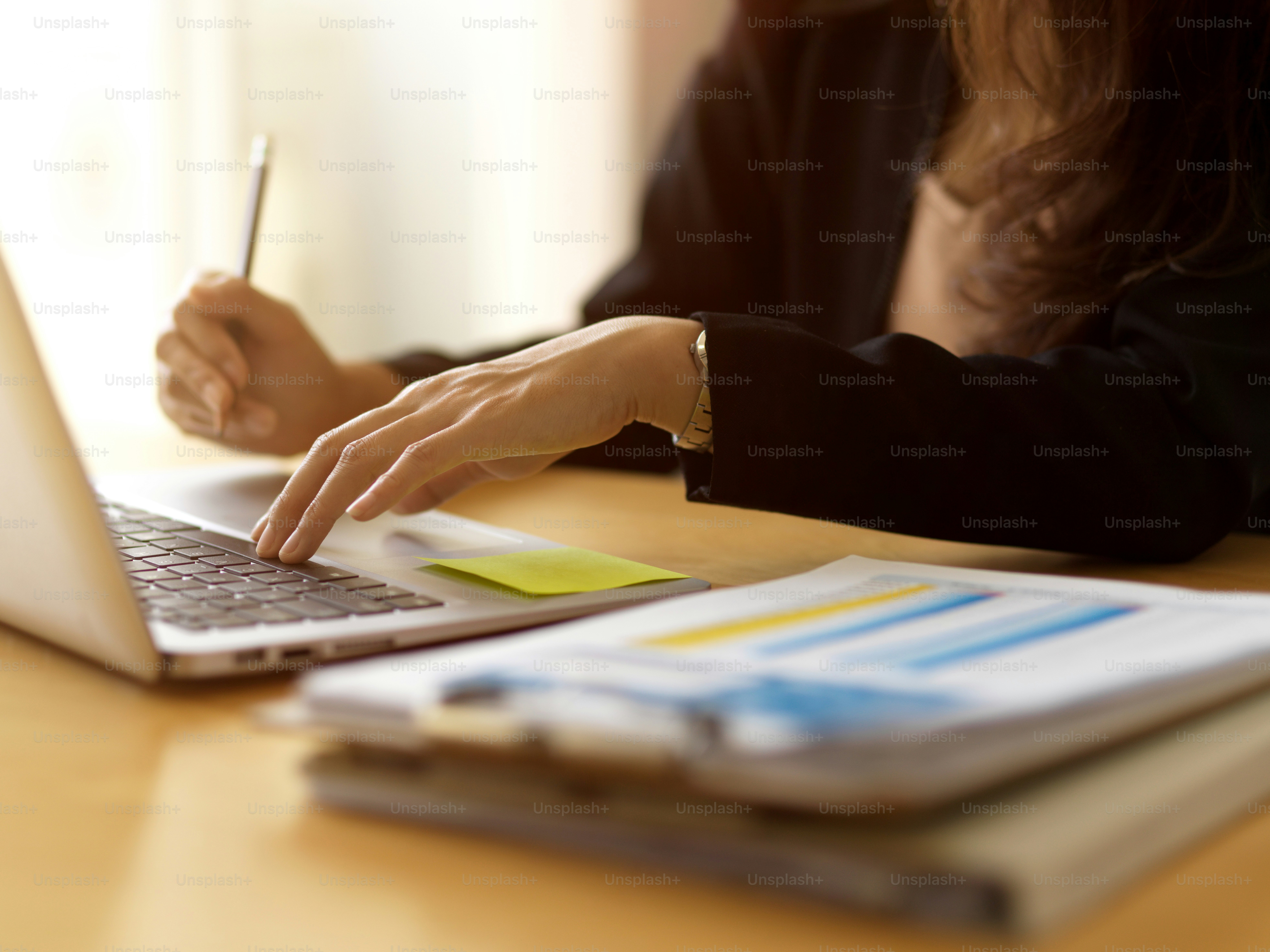 Nahaufnahme einer Geschäftsfrau bei der Arbeit mit Laptop und Papierkram auf einem Holztisch
