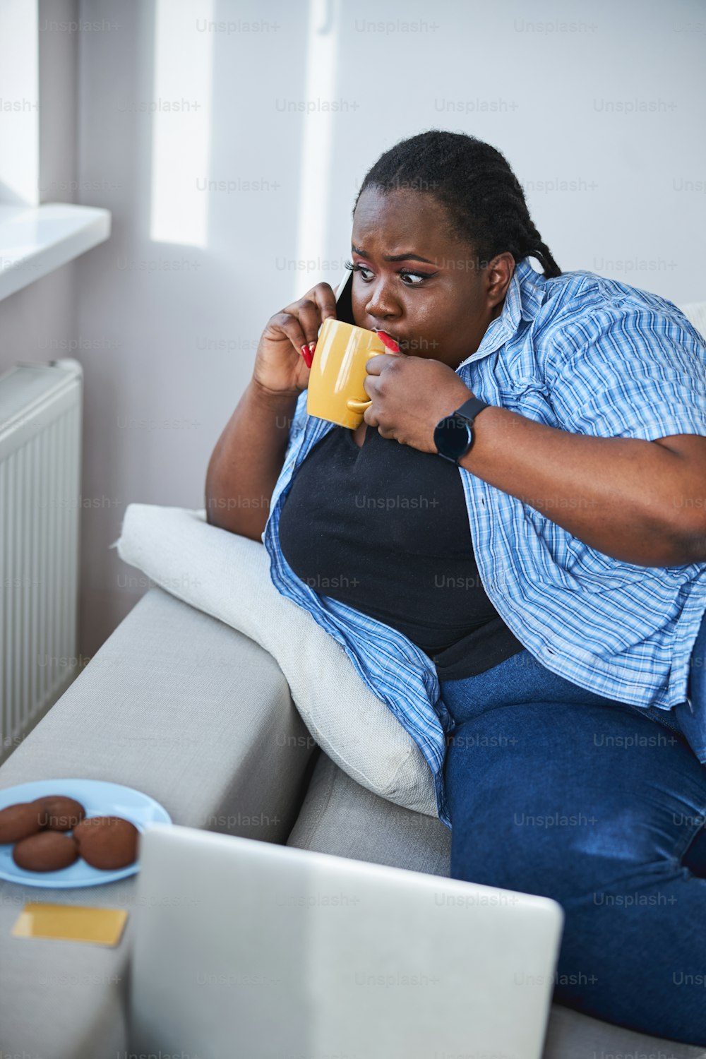 Afro-American woman looking somewhat terrified while sipping tea and talking on the phone